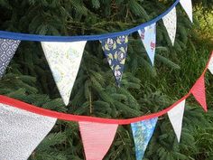 a bunch of flags hanging from a tree in the grass with pine trees behind them