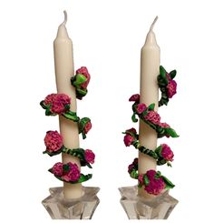 two white candles with pink flowers and green leaves on each candle holder, one is tall