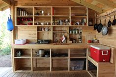 an outdoor kitchen with pots and pans hanging from the ceiling, on wooden flooring