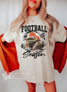 ✨ Football Season 🏈🧡 Get in the zone with our "Football Season" t-shirt! This design features a bold, trendy mix of collegiate and modern cursive fonts, with a striking orange football helmet and ball at the center. Surrounded by checkered flag icons and set against a grunge background, this tee captures the raw energy of the game.  Perfect for wearing to the stadium, tailgate parties, sports bars, or casual game day gatherings, it's a must-have for passionate fans who want to show their spiri Football Season Sports Fan T-shirt With Sublimation Print, Sports Fan T-shirt For Football Season, Football Season Sublimation Design T-shirt For Sports Events, Football Season Sublimation Design With Team Logo, Football Season Team Logo T-shirt, Football Season T-shirt With Team Logo, Team Spirit Sports T-shirt For Fall, Team-colored Sublimation Design With Team Logo For Football Season, Football Season Fan Apparel With Team Logo