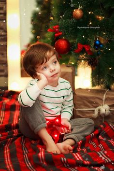 a little boy sitting on the floor next to a christmas tree