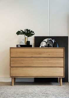 a wooden dresser sitting next to a plant on top of a hard wood flooring