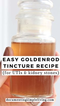 A light hand holding a small glass jar of goldenrod tincture.