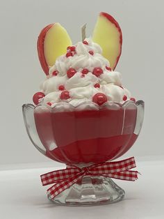 an apple dessert with whipped cream and cherries in a glass bowl on a white surface