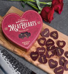 heart shaped cookies sitting on top of a cutting board next to a knife and roses