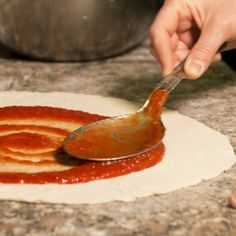 a person using a knife to spread sauce on pizza dough