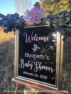 a welcome sign for a baby shower is displayed on a easel in the grass