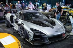 a silver sports car is on display at an auto show with people looking around it