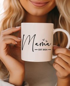 a woman holding a white coffee mug with the word mama printed on it in black