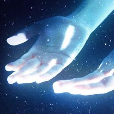 two white hands are glowing in the dark blue light, with snow flakes all around them