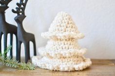 a crocheted christmas tree next to a black comb on a wooden table with pine needles