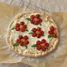 a pizza with tomatoes and flowers on it sitting on top of a piece of wax paper