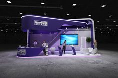 two people standing in front of a purple and white trade show booth with tvs