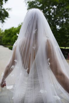 the back of a bride's veil with white flowers on it is seen from behind