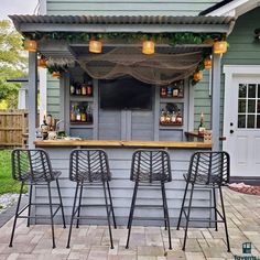 an outdoor bar with stools and bottles on the back wall, in front of a house