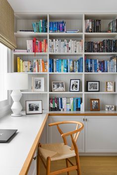 a white book shelf filled with lots of books next to a chair and desk in front of a window