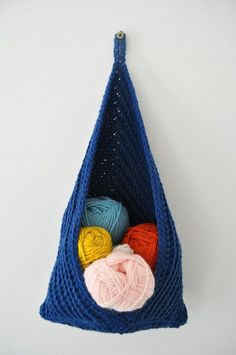 a blue crochet bag with balls of yarn in it hanging on the wall