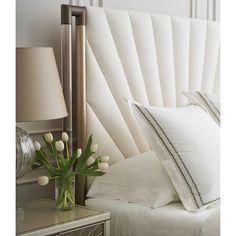 a bed with white pillows and tulips in a vase on the side table