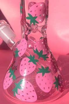 a glass vase with strawberries painted on the bottom and sides, in front of a pink background