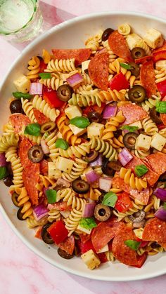 pasta salad with pepperoni, olives, tomatoes and other toppings in a white bowl