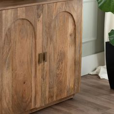 a wooden cabinet sitting on top of a hard wood floor next to a potted plant