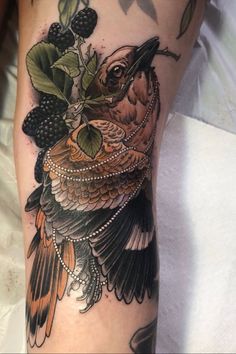 a bird with berries and leaves on it's leg is shown in this tattoo