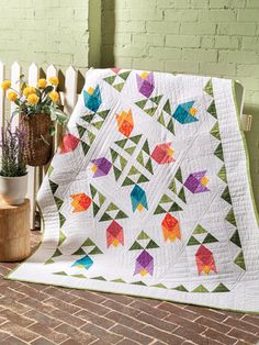 a colorful quilt sitting on top of a wooden table next to a potted plant