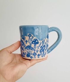 a hand holding a blue and white coffee cup with mushrooms on the inside, in front of a white background