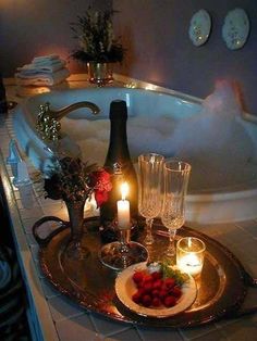 a bath tub filled with candles next to wine glasses and strawberries on a plate