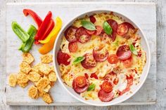 a pizza with pepperoni and cheese in a white bowl next to crackers and peppers