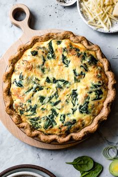 a quiche with cheese and spinach on a cutting board next to other dishes