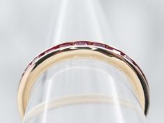 This is such an easy ring to wear! It sits low to the hand, and the sparkling synthetic ruby gemstones are set flush to the metal - there are no prongs to snag on this band! Crafted of 14-karat yellow gold, the flat sides will sit snug against an engagement ring, and stack with other bands with no gaps. *Please note, that one of the rubies is chipped and this piece has been priced accordingly.Metal: 14K Yellow GoldGem: Synthetic RubiesWidth of Band: 2.6 mmHeight off Finger: 2.1 mmRing Size: 5.50Marks: "14K" Stamped on the inside band Modern Yellow Gold Ruby Ring For Wedding, Ruby Ring With Polished Finish And Round Band, Gold Ruby Half Eternity Round Cut Ring, Formal Pink Gold Ruby Ring With Prong Setting, Gold Ruby Ring With Baguette Cut And Prong Setting, Gold Ruby Ring Half Eternity Style, Yellow Gold Ruby Ring With Baguette Cut, Gold Ruby Ring With Half Eternity Design, Yellow Gold Ruby Half Eternity Ring