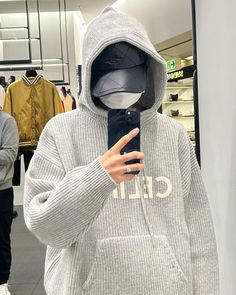 a person in a gray hoodie taking a selfie with a cell phone and wearing a mask