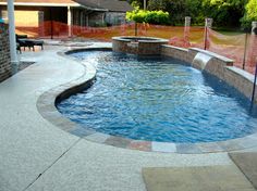 an outdoor swimming pool surrounded by stone steps and fenced in area with fire pit