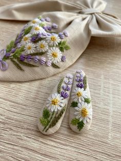 two white slippers with purple and yellow flowers on them next to a beige cloth bag