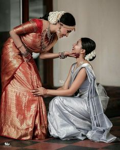 two women dressed in silver and one wearing an orange sari with her hand on the other's shoulder