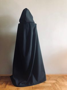 a black cloak sitting on top of a hard wood floor next to a white wall