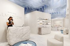 a woman standing in front of a counter at a beauty store with white walls and blue ceiling