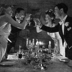 black and white photograph of people toasting at a dinner table with candles in the background