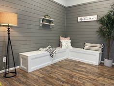 a room with wood flooring and gray walls has a white bench on the far wall