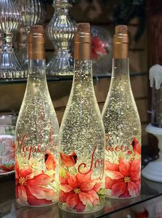 three wine bottles with flowers painted on them are sitting on a glass table in front of other items