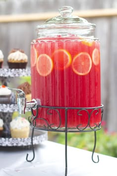 a glass jar filled with red liquid next to cupcakes