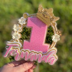 a hand holding up a pink and gold number one sticker with flowers on it