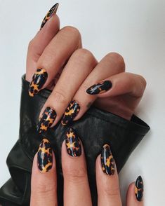 a woman's hand with black and orange leopard print nail art designs on it