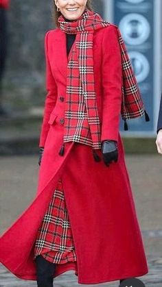 the woman is wearing a red coat and black boots while she walks down the street