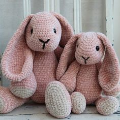 two crocheted pink stuffed animals sitting next to each other on a white chair