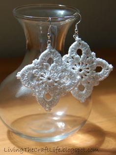 white crocheted lace earrings in front of a glass vase on a wooden table