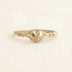 a gold ring with a heart and two small diamonds on the front, sitting on a white surface