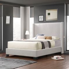 a white bed sitting on top of a hard wood floor next to a large window