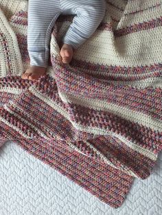 a baby laying on top of a bed next to a knitted blanket and pillow